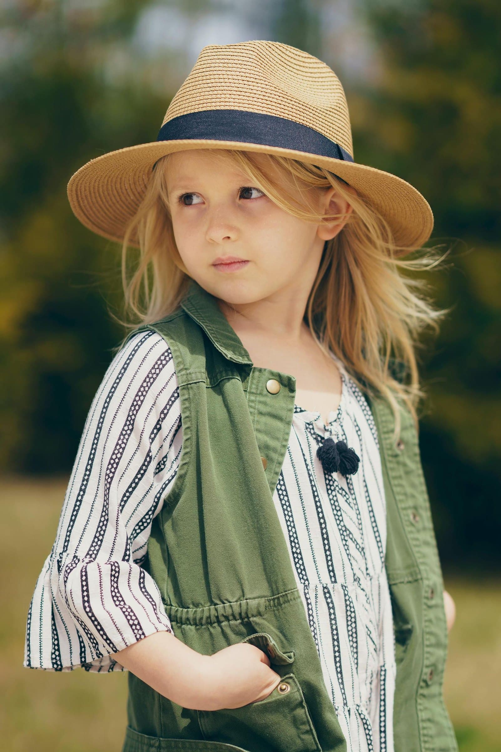 Young girl in a straw hat and green vest glancing to the side in a sunlit field