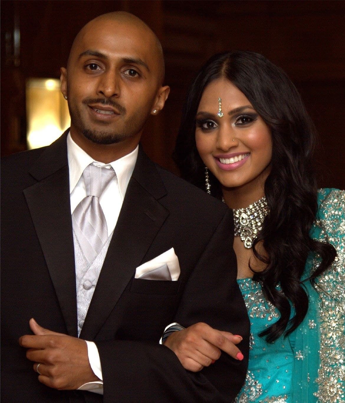 Couple walking arm in arm at their reception, the groom in a black tuxedo and the bride in a turquoise embellished outfit